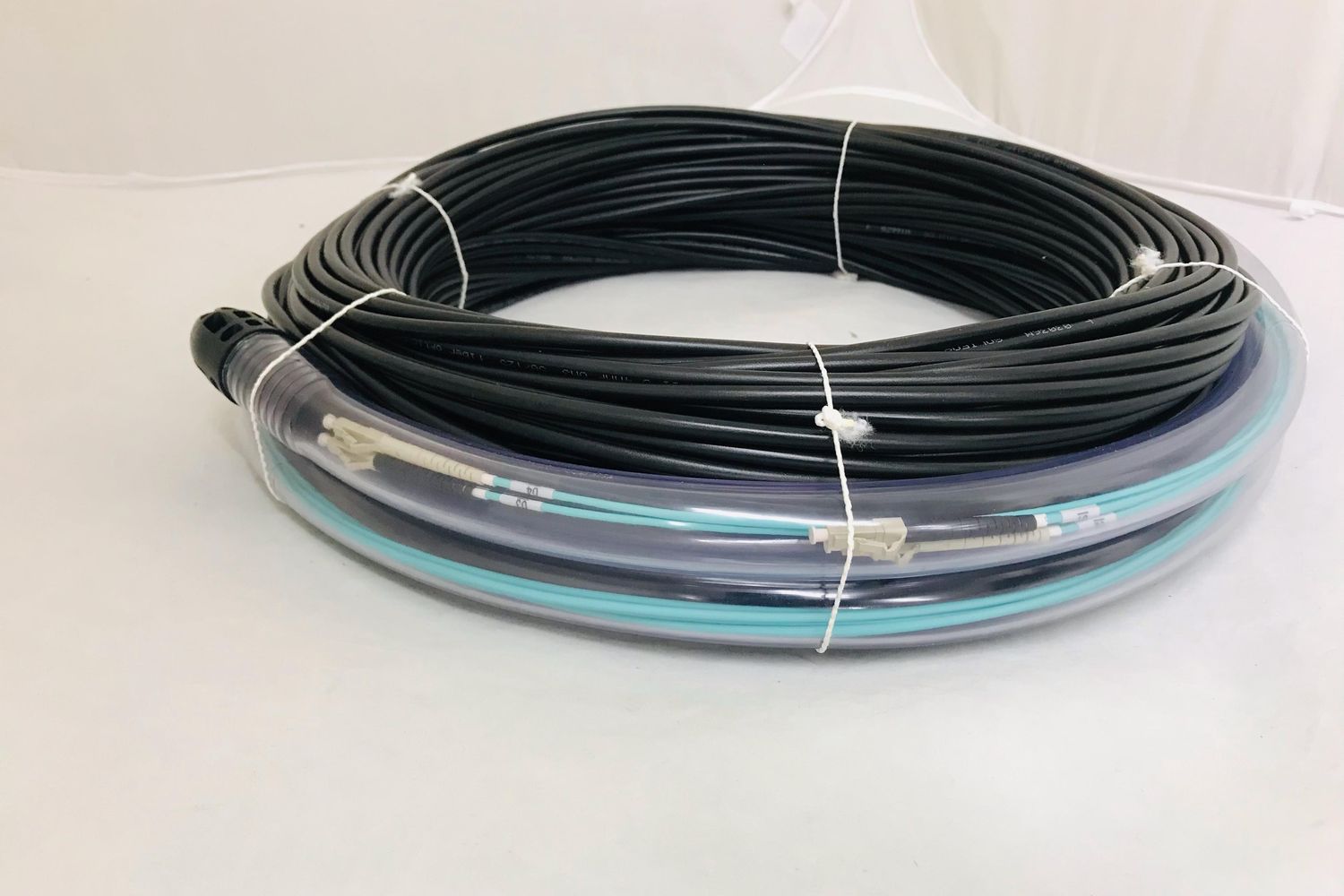 Coiled black Mil-Tac fibre cable assembly with the connector ends protected in clear tubing